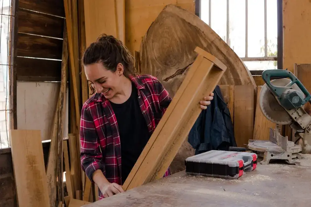 Une menuisière sourit en ajustant une planche de bois dans son atelier