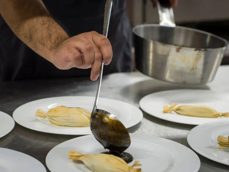 Un chef nappe de sauce des assiettes alignées sur le passe, en cuisine