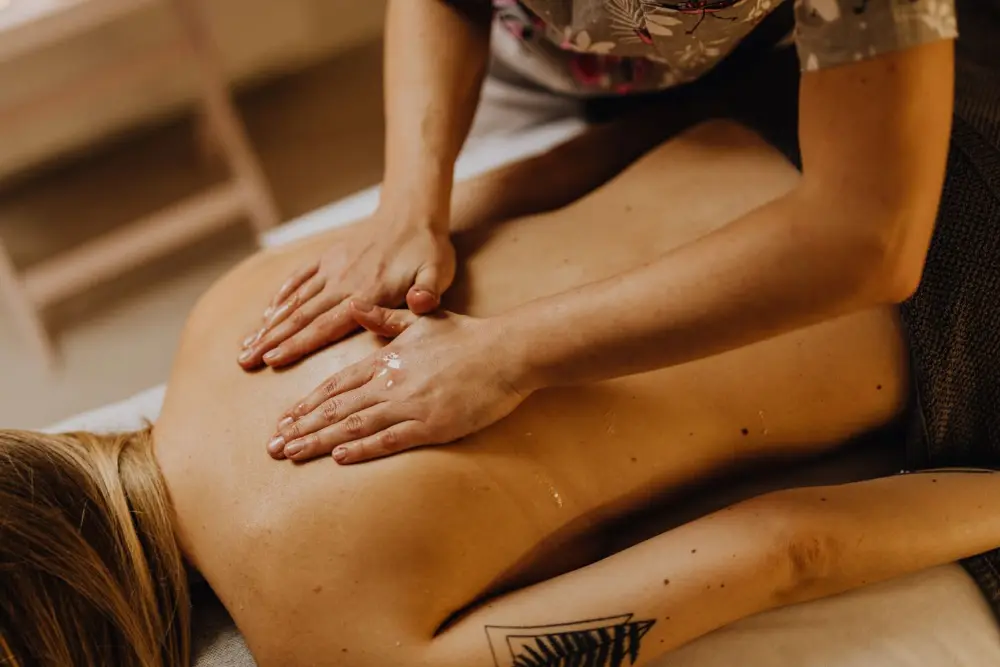 Les mains d’une masseuse massent le dos d’une cliente allongée sur une table de massage